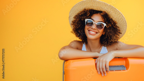 Smiling woman ready for adventure, leaning on an orange suitcase, passport in hand, against a sunny yellow background.