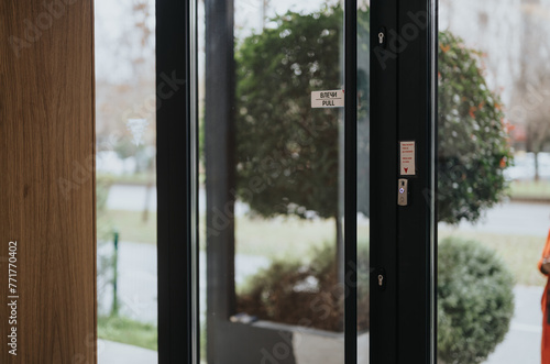 View through a contemporary glass door marked with pull signs and equipped with electronic access control panels on a bright day.