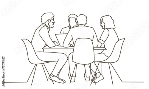 A group of people are sitting around a table  with one person using a laptop