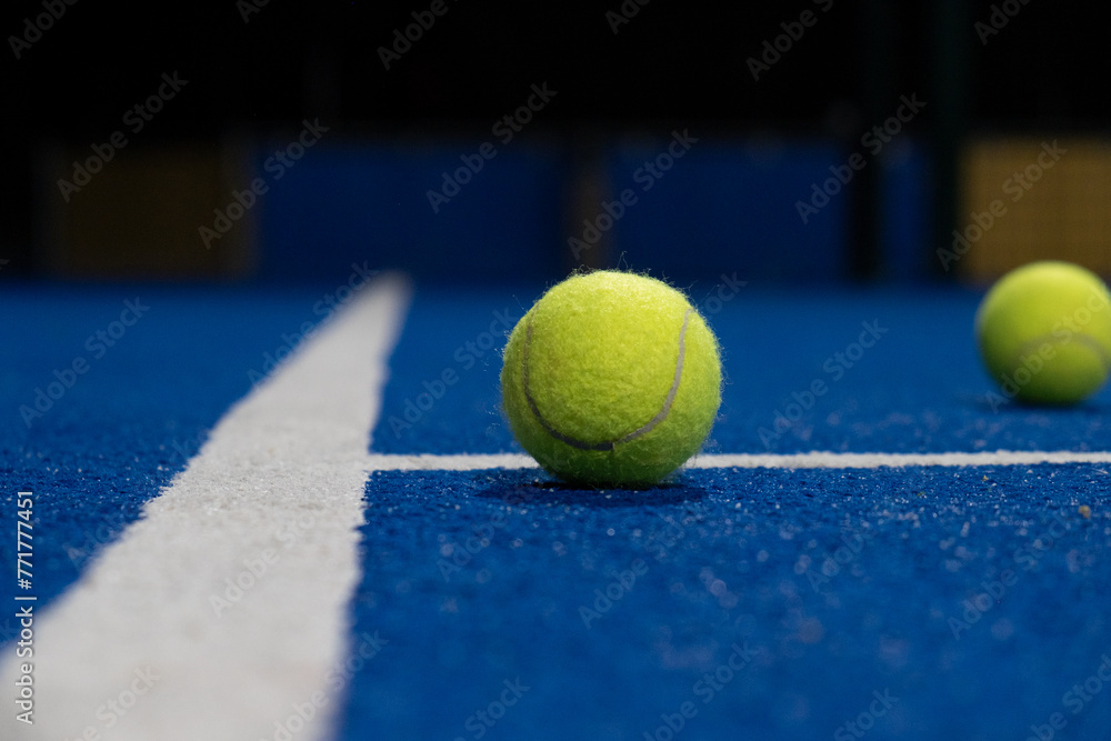 Selective focus, two balls and the line of a blue paddle tennis court at night