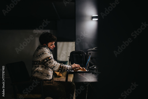 A solitary man concentrated on work using his laptop late at night in a dimly lit environment, illustrating dedication, overtime, and solitude at work.
