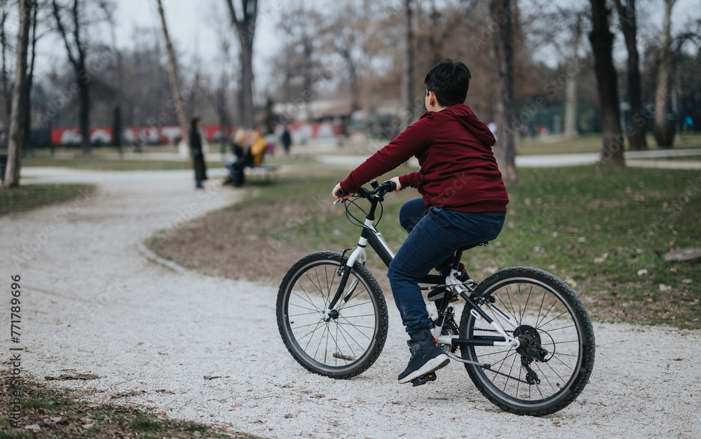 A boy enjoys cycling on a gravel path in a city park, surrounded by lush greenery and breathing fresh air.