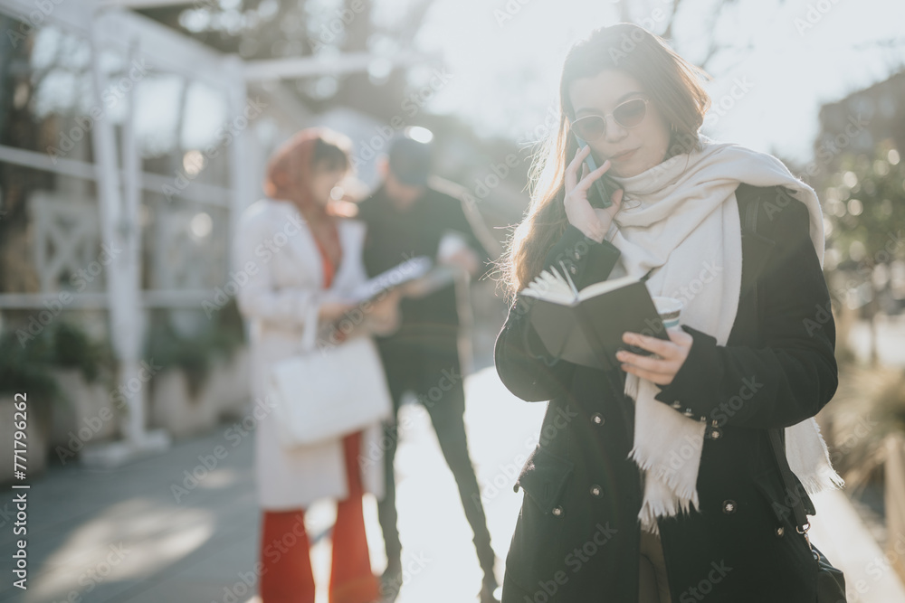Stylish urban woman multitasking with a smart phone in one hand and writing in a notebook, with friends in the background. Stylish urban woman multitasking with a smart phone in one hand and writing in a notebook, with friends in the background.