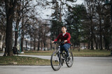 A happy boy rides his bicycle through a leafy urban park, enjoying the freedom and joy of a relaxing weekend outdoors.