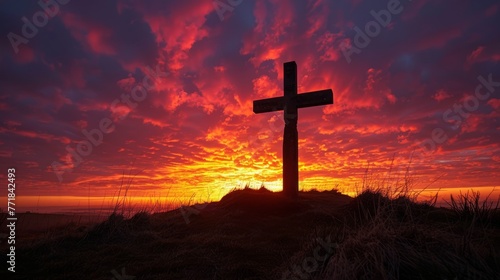 Stark silhouette of the Easter cross against a fiery sunset sky, atop a hill, a beacon of faith © saichon