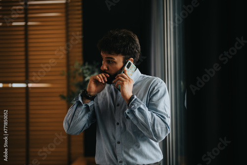 A focused business entrepreneur in a casual shirt engaged in a serious phone conversation