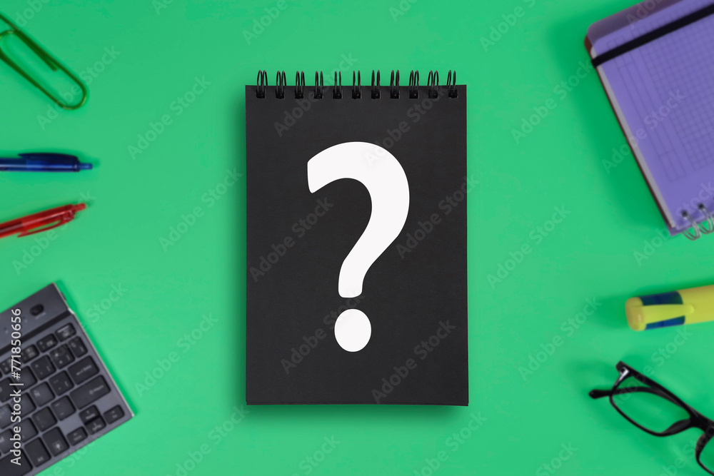 Question. White question mark on a black notepad. Blurred green background with school items. Concept of finding a solution, confusion, decision making, choice, problem. Question. White question mark on a black notepad. Blurred green background with school items. Concept of finding a solution, confusion, decision making, choice, problem.