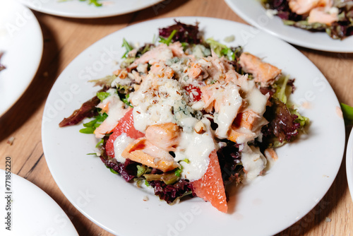 Gourmet Salad with Smoked Salmon and Cheese. Close-up of a gourmet salad with smoked salmon, grated cheese, mixed greens, and grapefruit slices, served on a white plate.