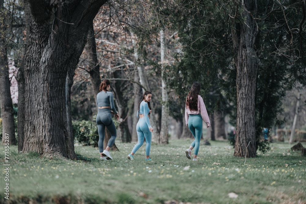 Fototapeta premium Three female athletes in sportswear exercising by jogging in a serene park setting, showcasing teamwork and dedication to fitness.