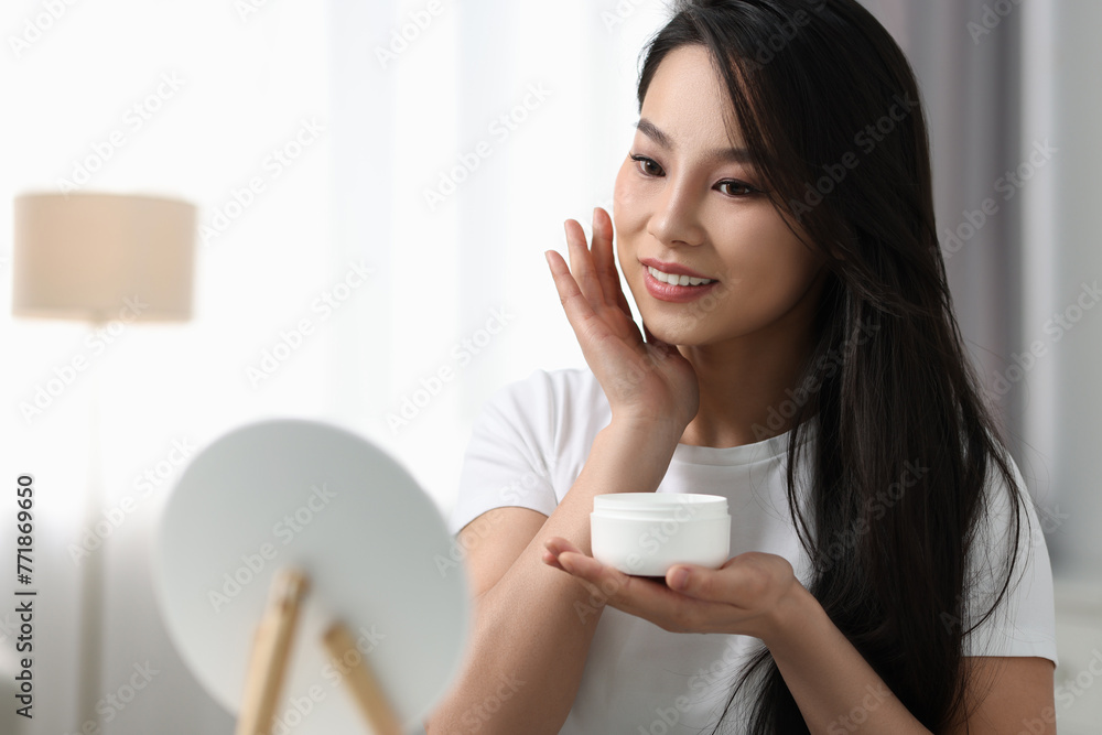 Happy woman applying face cream at home, space for text Happy woman applying face cream at home, space for text