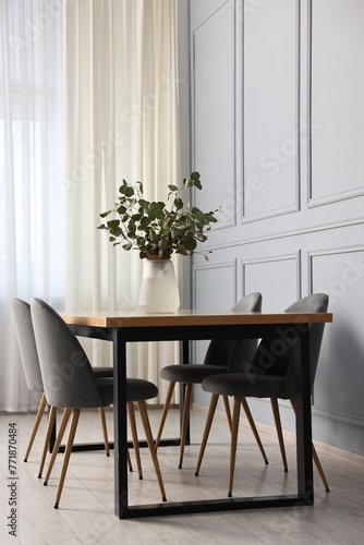 Soft chairs, table and vase with eucalyptus branches in stylish dining room