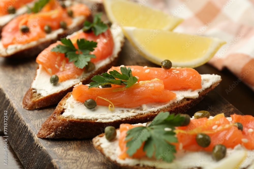 Tasty canapes with salmon, capers, lemon and cream cheese on wooden board, closeup