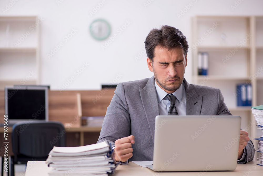 Young male employee unhappy with excessive work in the office Young male employee unhappy with excessive work in the office