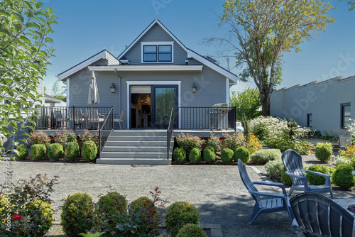 A charming gray traditional cottage with a welcoming outdoor patio, enveloped by verdant plants and shrubs.