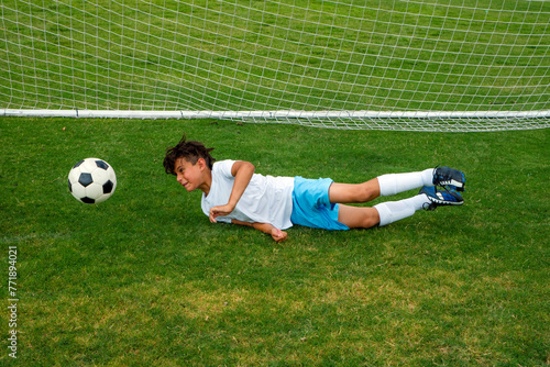 Male youth soccer goalie diving to the ground to block a shot on goal