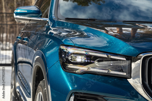 Headlight of a modern popular blue car close-up. Shiny glass car headlight with glare from lighting.