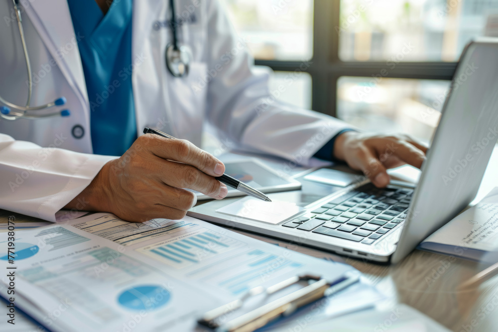 A medicine doctor working on a digital tablet and laptop computer, searching for information with medical documents on the table. Close-up view of the doctor writing prescriptions and filling out heal A medicine doctor working on a digital tablet and laptop computer, searching for information with medical documents on the table. Close-up view of the doctor writing prescriptions and filling out heal