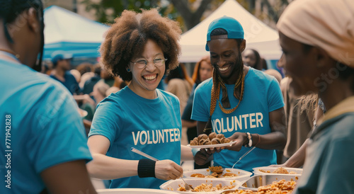 A group of diverse people wearing light blue t-shirts with  VOLUNTEER  written on them  serving food to the homeless at outdoor 