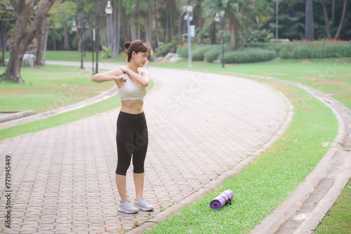 Shoulder pain problem. woman jogger. 30s asian female wearing white sportswear holding her shoulder with pain after running exercise in public park.
