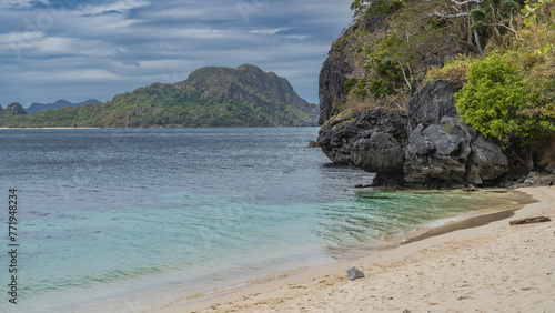 A secluded sandy beach on a tropical island. A calm turquoise ocean. Green vegetation on picturesque coastal cliffs. A mountain on a background of blue sky and clouds. Philippines. Palawan. El Nido © Вера 