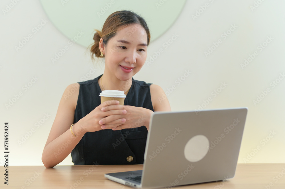 Smiling Woman Enjoying Coffee While Working on Laptop Smiling Woman Enjoying Coffee While Working on Laptop