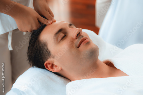 Caucasian man enjoying relaxing anti-stress head massage and pampering facial beauty skin recreation leisure in dayspa modern light ambient at luxury resort or hotel spa salon. Quiescent