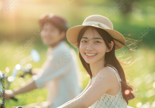 A young asian couple riding bicycles in a summer park, smiling and having fun together on a romantic date
