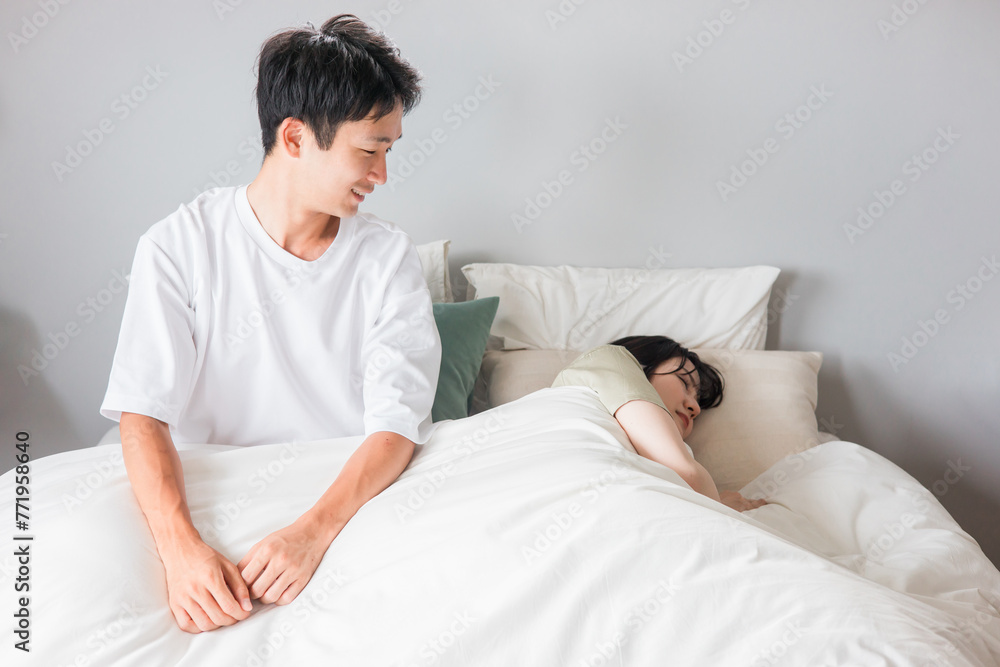 Fototapeta premium ベッドで熟睡・睡眠・快眠している妻を笑顔で見つめる夫・男性