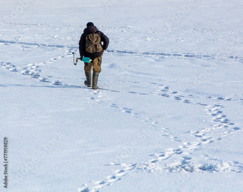 A man fisherman with an ice auger in his hands leads through the white snow in winter