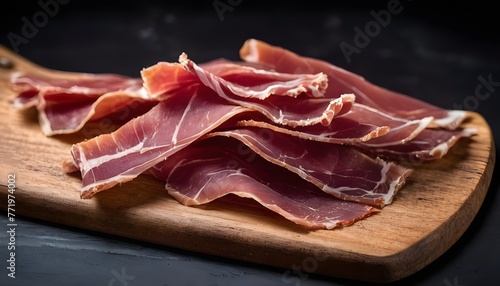 Pieces of dried pork prosciutto on a wooden board. black background