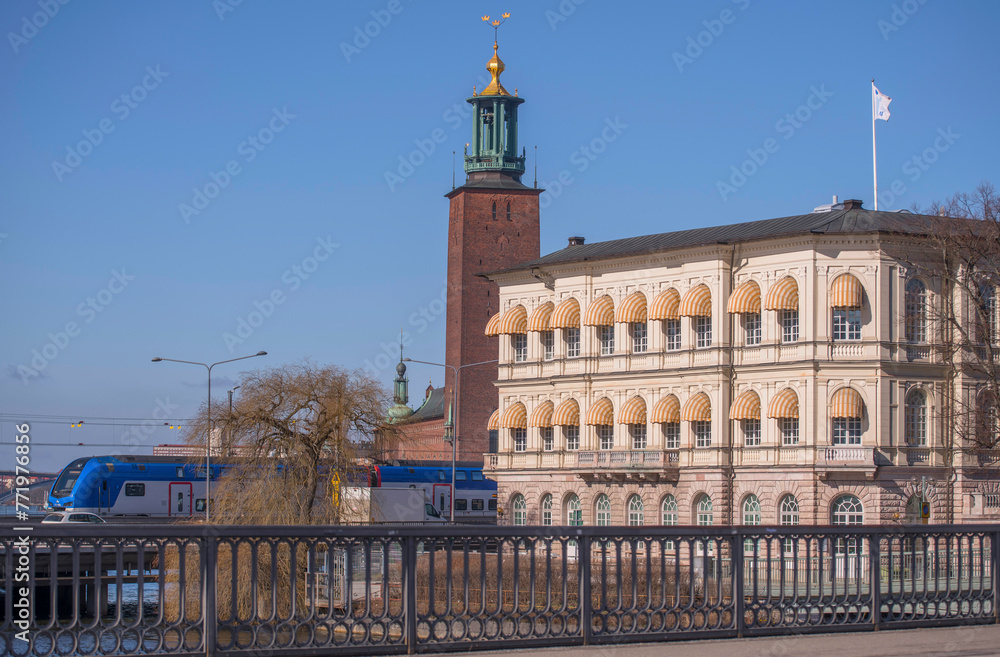 Commuter train arriving, the Town City Hall, an old yellow office building in the island Strömsborg in Stockholm a sunny spring day