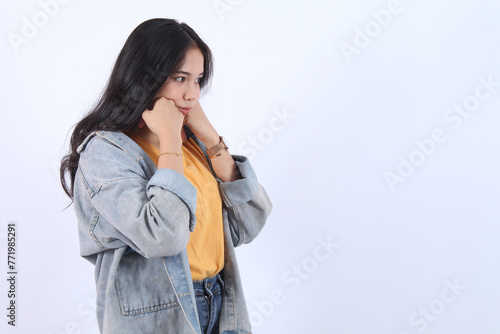 Young pensive sad woman of Asian ethnicity 20s with holding chin and sulking disappointed crying stand white background bothered. People lifestyle concept © Miftakhul Fariz