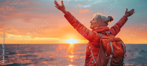 Confident mature woman with backpack with arms up relaxing at sunset seaside during a trip , old female traveler enjoying freedom in serene nature landscape