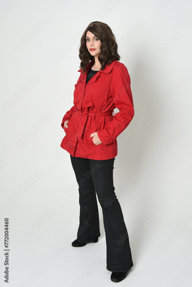 full length portrait of beautiful brunette woman model, wearing red trench coat jacket leather pants. standing pose, walking towards the camera. isolated on white studio background.