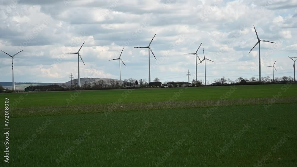 Rotating propellers of a wind farm behind a green field.