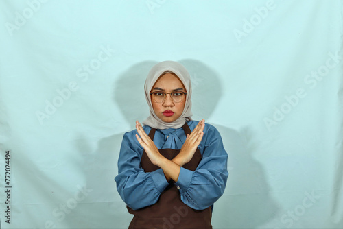 housewife woman in hijab, glasses and brown apron doing stop gesture with crossed hands look at camera isolated on white background. People housewife muslim lifestyle concept 