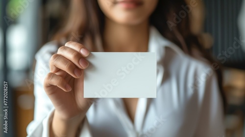 Mockup with beautiful manicured hands holding a 5 inches wide by 7 inches length, blank invitation card vertically, light background.