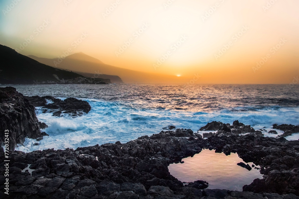 View of the landscape at sunset on the north coast of Tenerife with the Teide in the background on a day of haze with the sun reflected in a pool of lava View of the landscape at sunset on the north coast of Tenerife with the Teide in the background on a day of haze with the sun reflected in a pool of lava