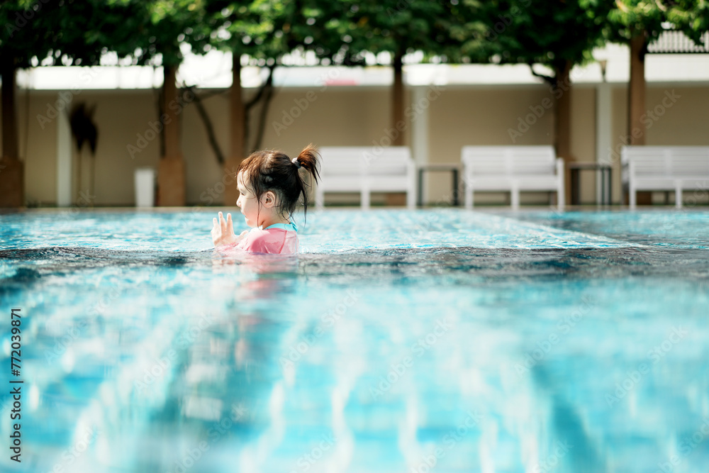 A little asian girl in swimming in the pool. Cute girl playing in outdoor swimming pool on a hot summer day. Kids learn to swim.