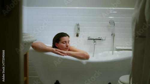 A young girl takes a bath. Girl relaxing after work in a hot bath. White bath. Hotel room. Shower. Taking a shower. Wet hair. Washing the head. Water. Bathroom. High quality 4k footage