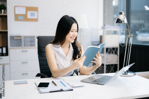 Asian woman reading book while sitting at  in cafe or home office.