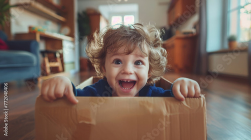 A young boy with a radiant smile is peeking out from a cardboard box. © Alena