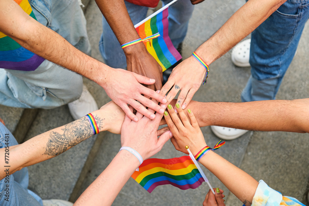 Obraz premium A group of people stacking hands and holding rainbow flags. Scene is one of unity and support for the LGBTQ community.