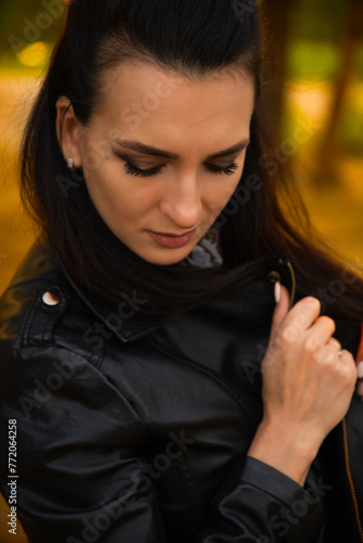 Portrait of a beautiful dark-haired young woman, girl on a background of summer sunset and a green park.