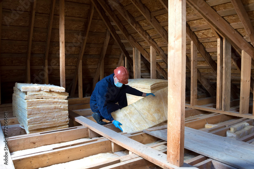 Roof insulation. A worker puts glass wool insulation in the attic.
