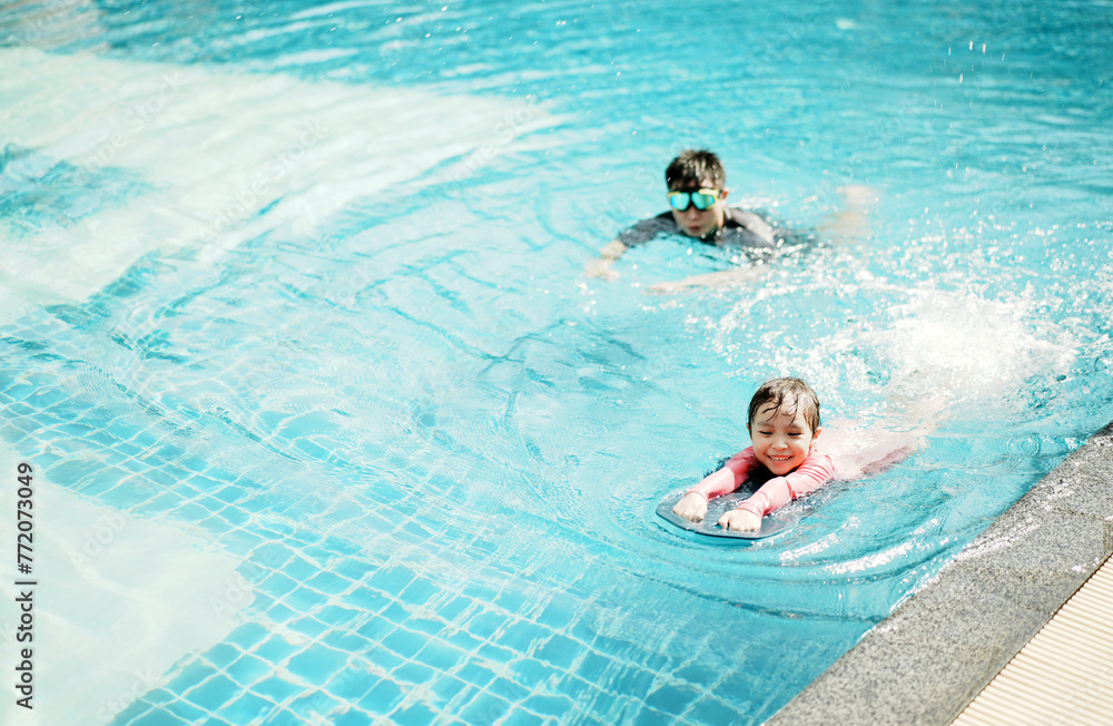 A little asian boy and girl in swimming in the pool. Cute girl playing in outdoor swimming pool on a hot summer day. Kids learn to swim.