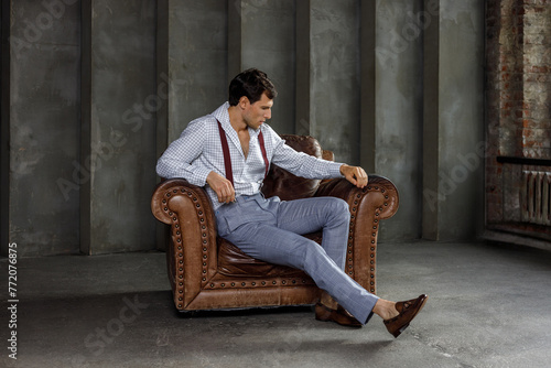 A young businessman is thinking after a meeting, posing in front of the camera in business formal clothes, sitting on an armchair