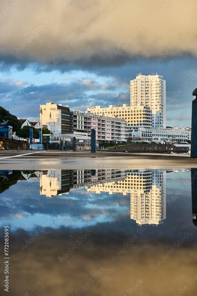 A hotel reflected in a puddle on a sunny day by the beach