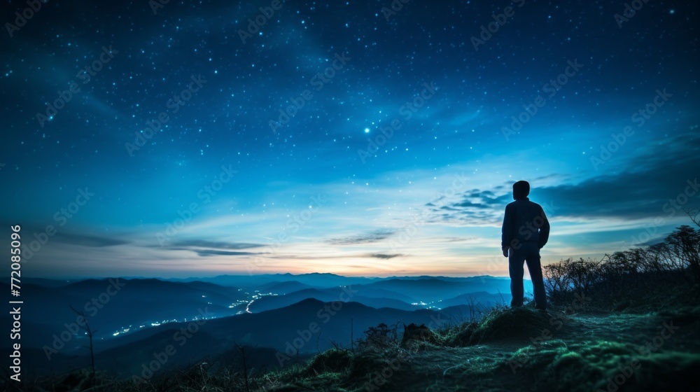 A man stands on a hill looking out at the stars