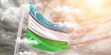 Uzbekistan national flag cloth fabric waving on beautiful cloudy Background.